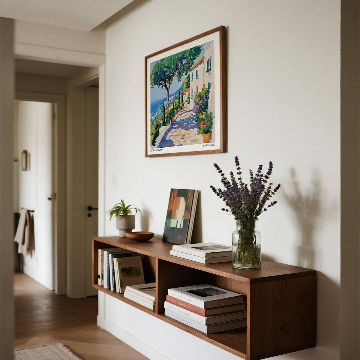 Prints of Amalfi Coast showing a Mediterranean path with trees and houses in vibrant watercolour hung above a wooden shelf with books