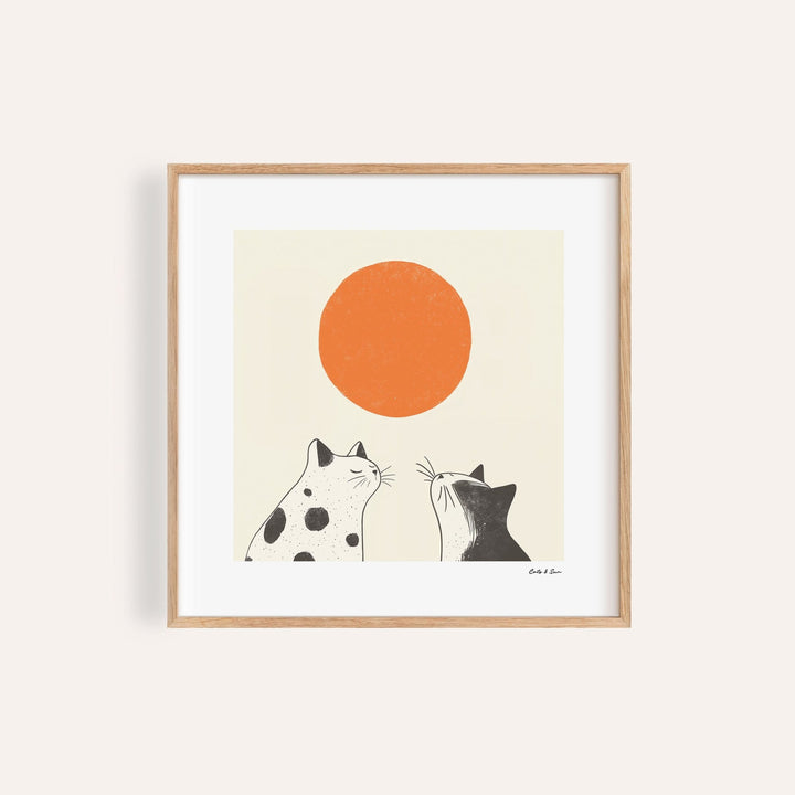 Framed print close-up of minimalist black and white cats looking at an orange sun
