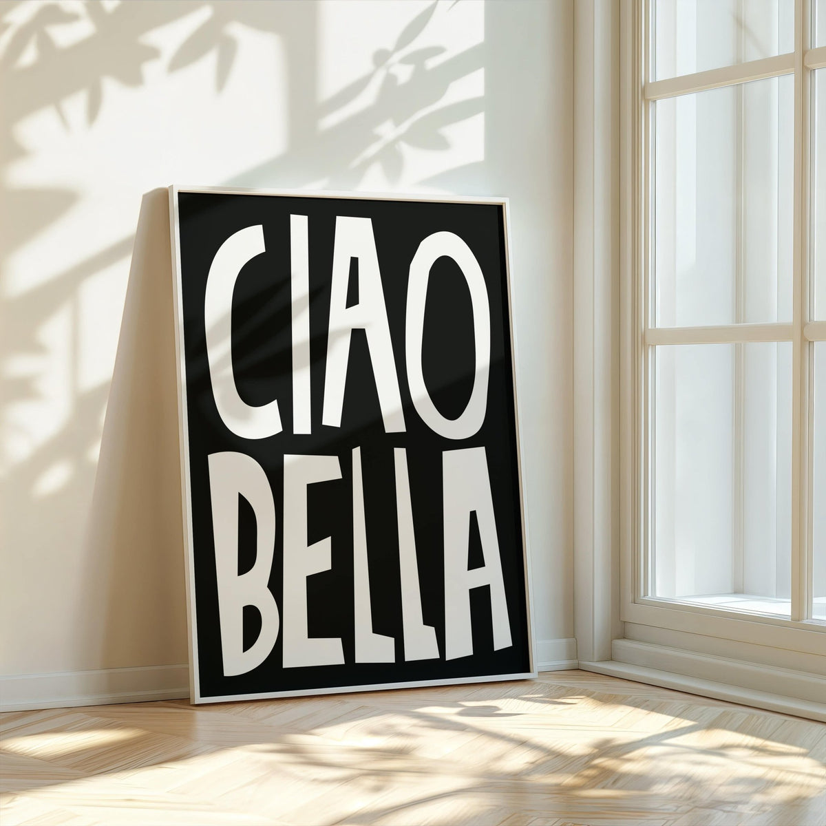 Typography wall art with white ciao bella text on black leaning against a white wall near a window