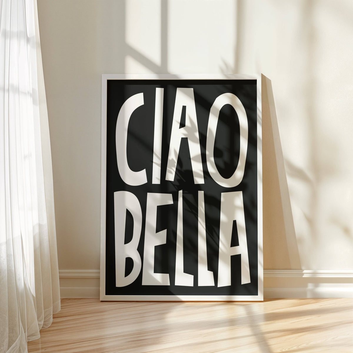 Typography wall art with ciao bella text in black and white leaning on a wooden floor near a sheer curtain