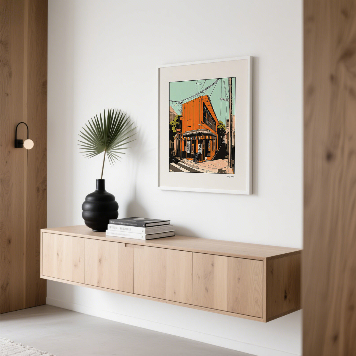 Tokyo wall art of orange street building hung above a wooden sideboard with a black vase