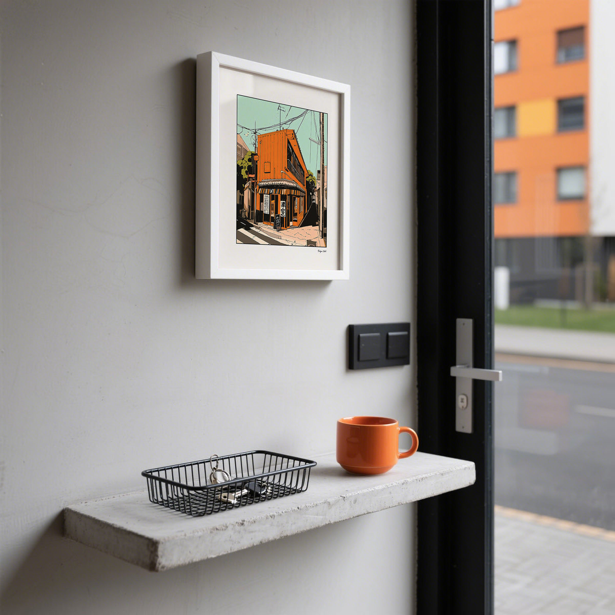 Framed Tokyo wall art of an orange street building above a shelf with an orange mug beside a door