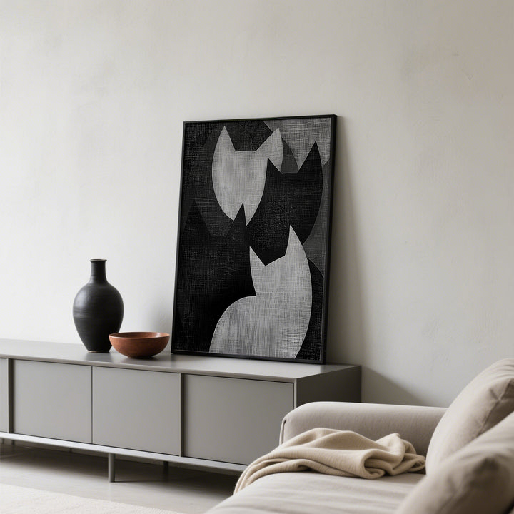 Print leaning on a sideboard of abstract cat shapes in black and grey with a black vase nearby