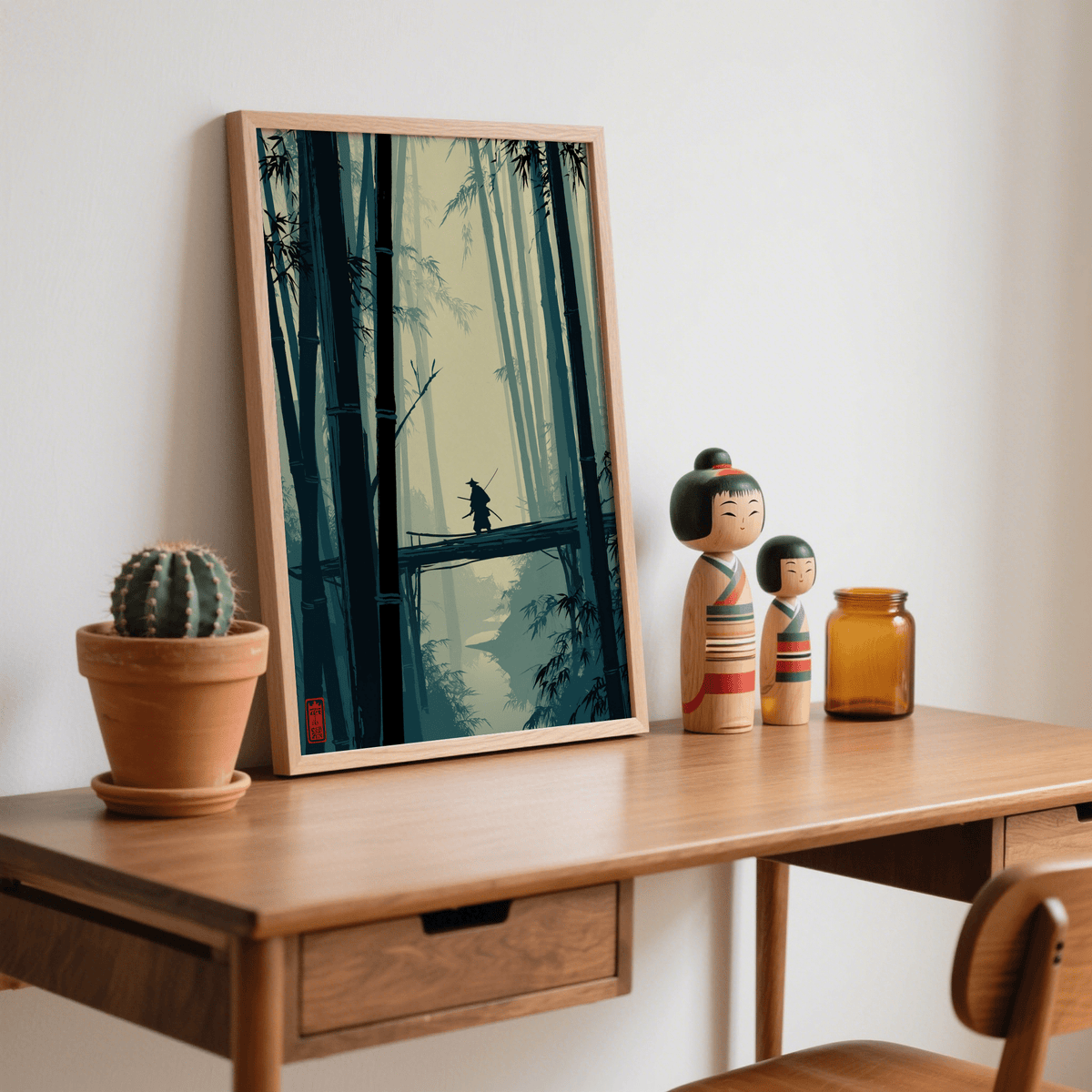 Japanese Bamboo Art Print leaning on a wooden desk next to two Japanese dolls and a cactus
