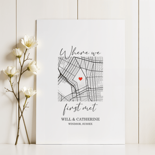 Heart on Map Print leaning on a white surface next to white flowers with a black and red minimalist map