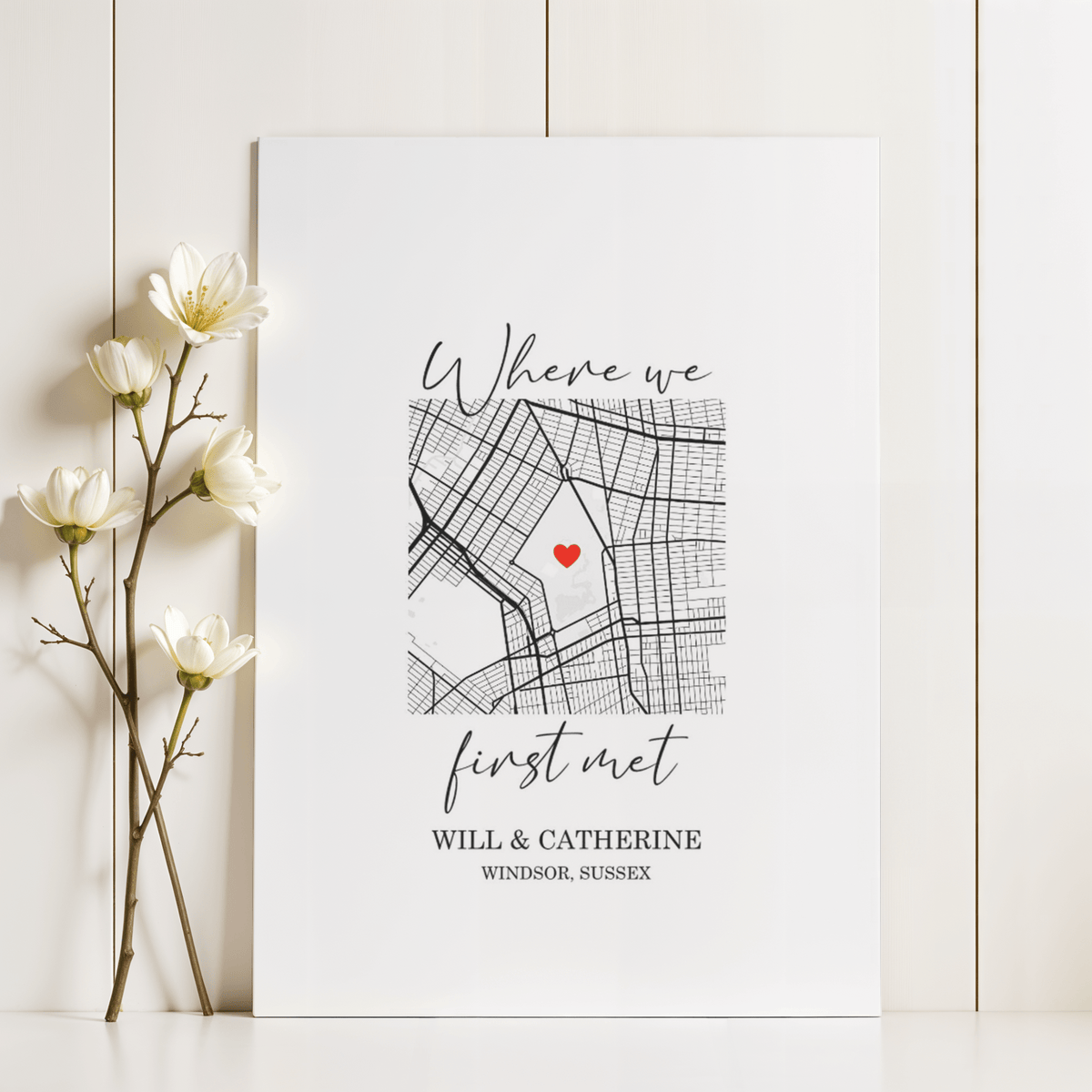 Heart on Map Print leaning on a white surface next to white flowers with a black and red minimalist map