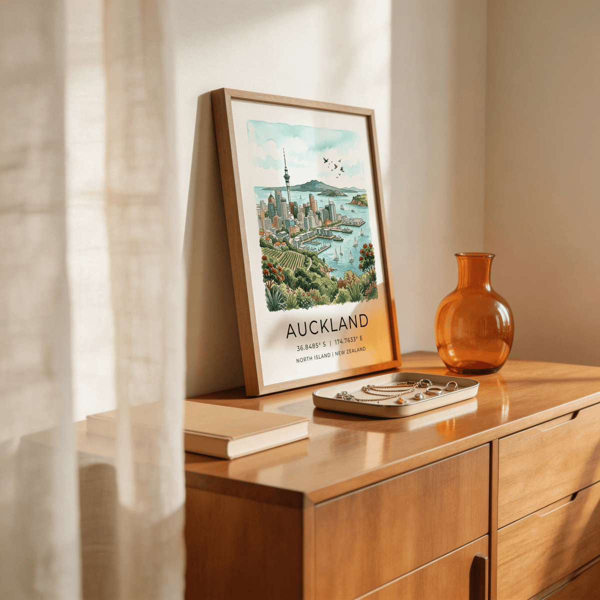 Print leaning on a sideboard of Auckland City art print with watercolour skyline and distant birds and sky beside an amber glass vase