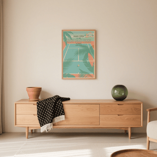 Print on a wall in a living room showing a pastel blue and peach tennis court with palm trees above a sideboard with green vase