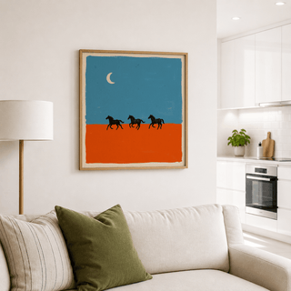 Horse silhouette wall art of three running horses against a blue sky with a crescent moon above a sofa with cushions