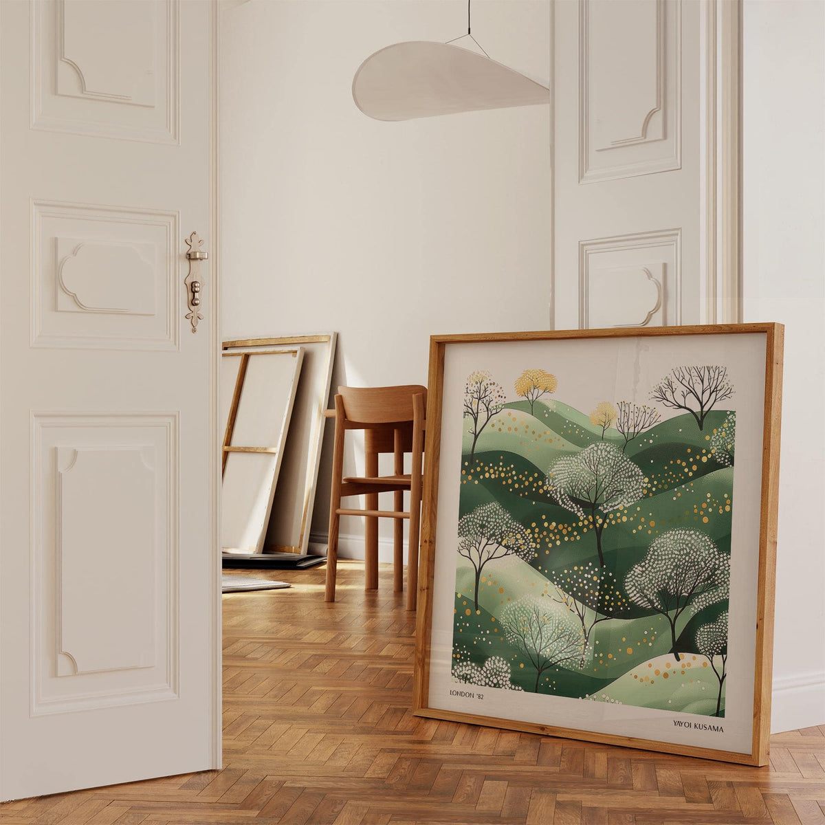 Wall Art Green print leaning on a parquet floor with white walls and a wooden chair in the background