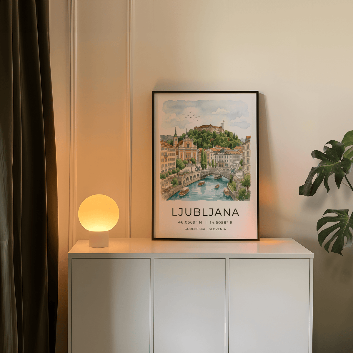 Ljubljana art print leaning on a white cabinet near a glowing spherical lamp and green plant