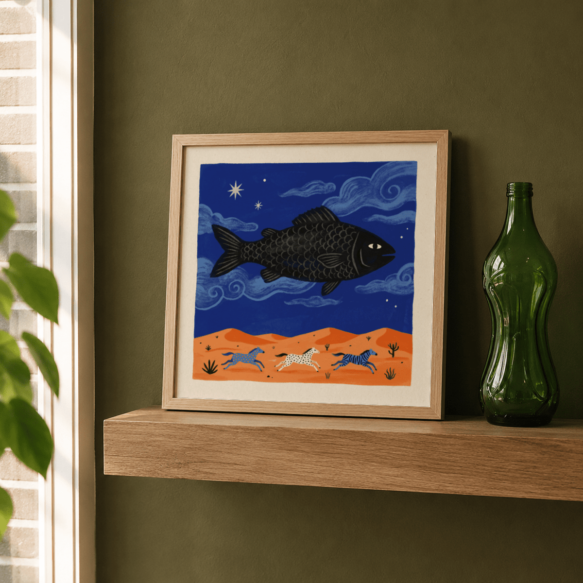 Whimsical Fish art print of a flying black fish above three horses on a desert landscape on a wooden shelf next to a green bottle