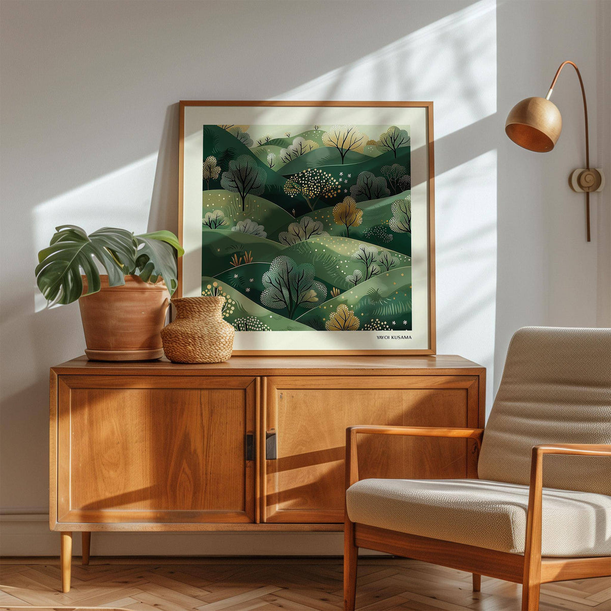 Large nature wall art with green hills and trees leaning on a wooden sideboard next to a potted plant