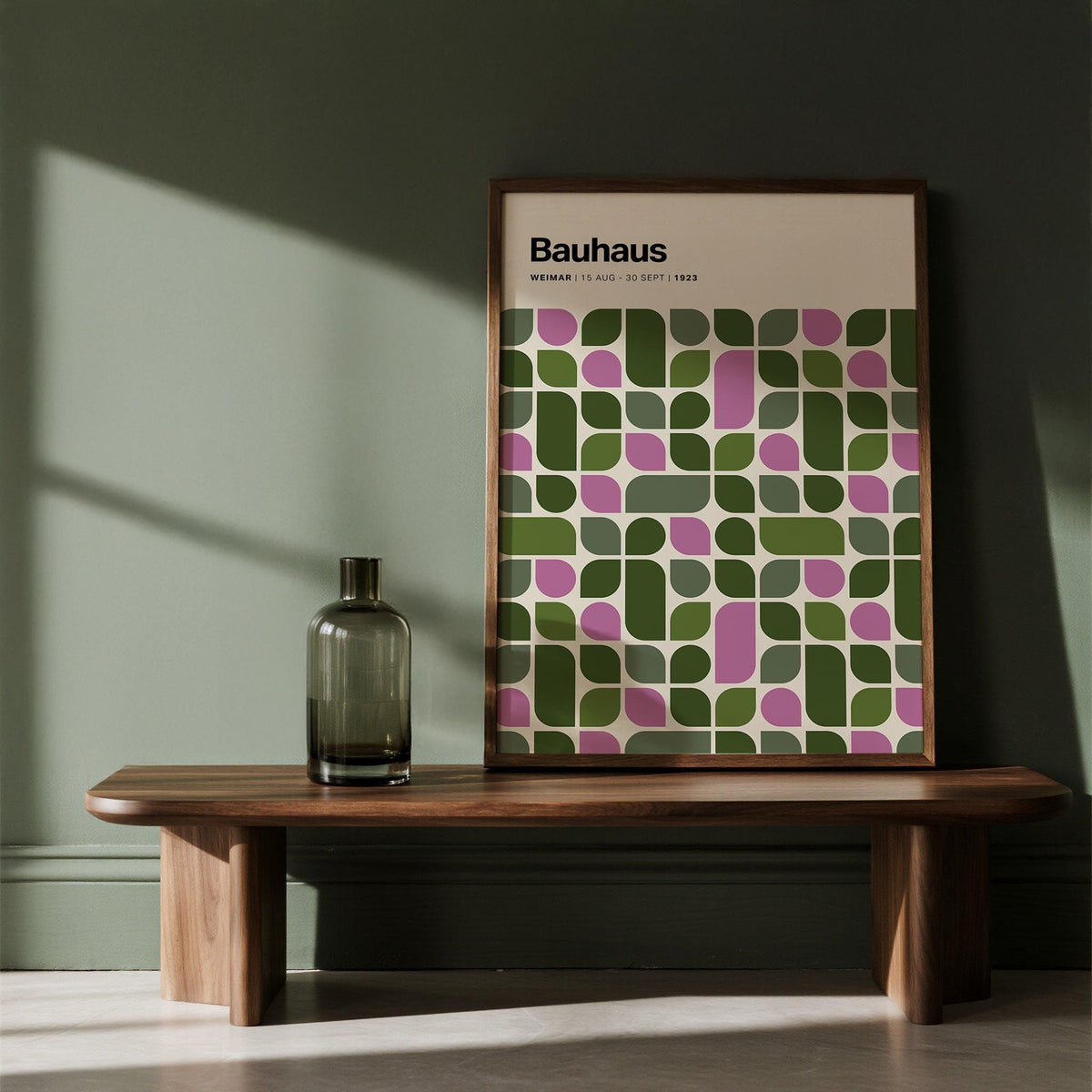 Print leaning on a shelf of geometric leaves pattern in pink and green against a dark green wall