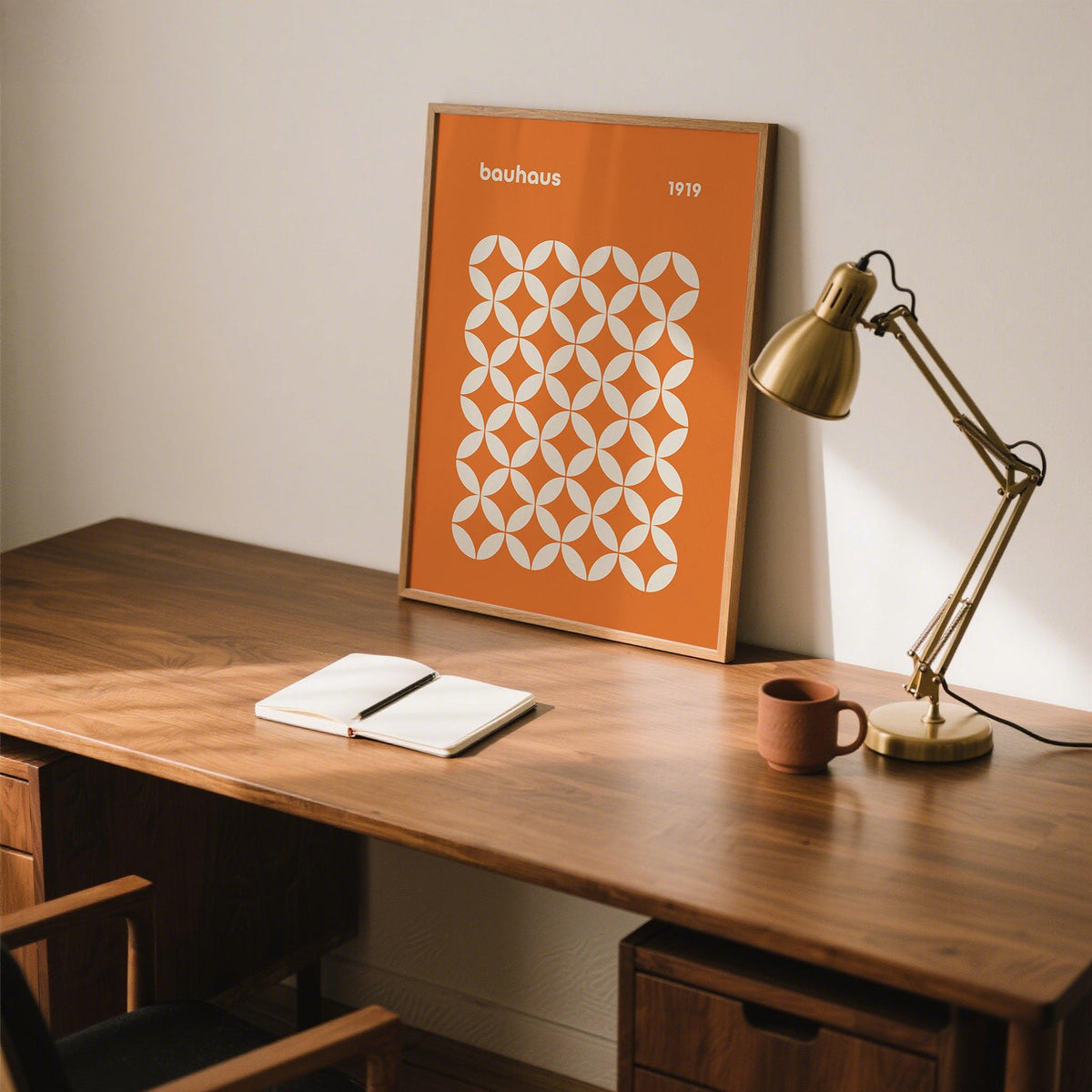 Orange poster framed print with a white circle grid pattern leaning on a desk with a brass lamp and terracotta cup
