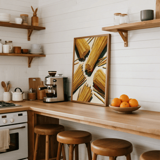 Spaghetti wall art leaning on a kitchen counter with wooden stools and a bowl of oranges