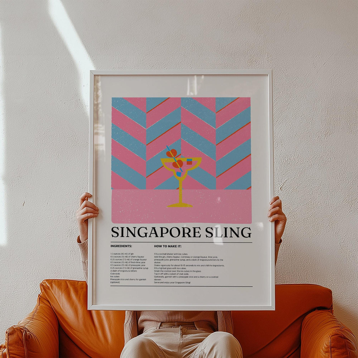 Framed print of Drinks Art Singapore Sling with a pink and blue chevron background held above a tan leather sofa