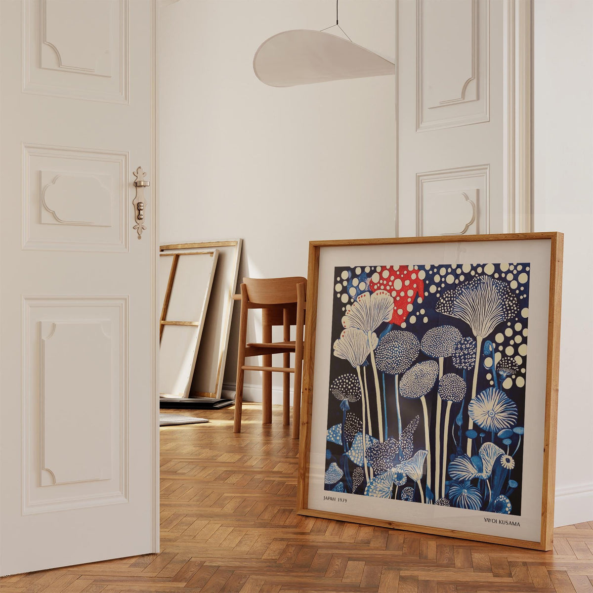 Red and Blue Art leaning on parquet floor with chair and stacked frames in the background