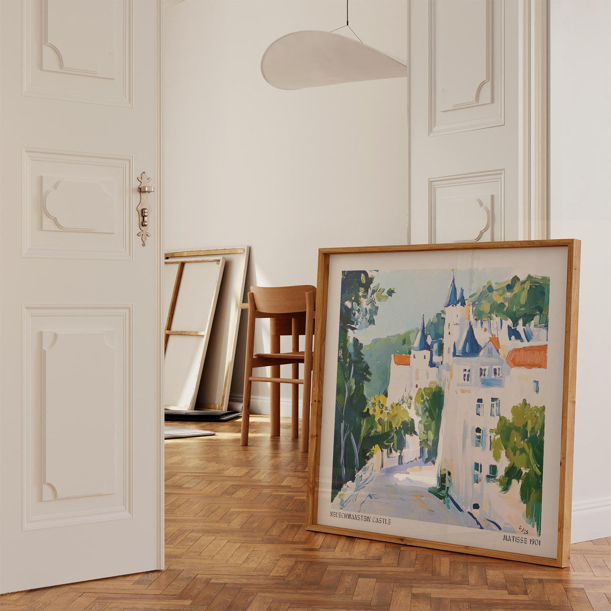 Print leaning on wooden floor depicting a pastel coloured castle with green trees in a white room