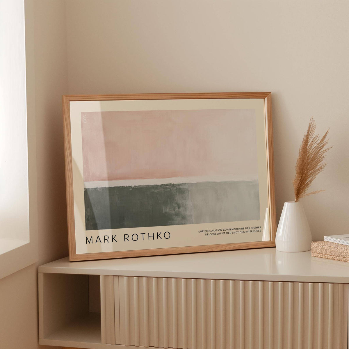 Framed horizontal wall decor with abstract faded pink and grey blocks leaning on a cream shelf next to a white vase
