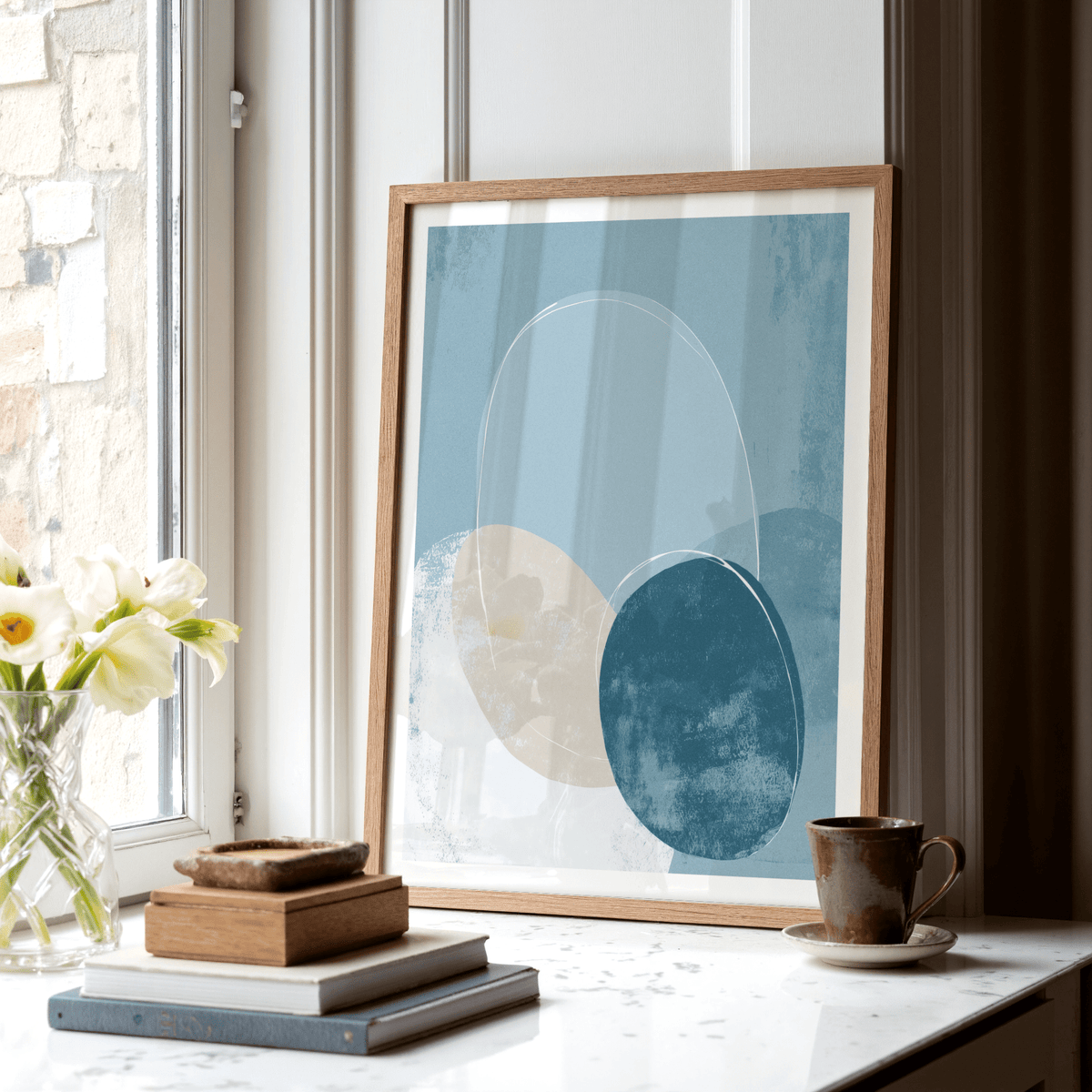 Geometric Circle Poster leaning on a windowsill with white and blue abstract ovals and a brown cup nearby