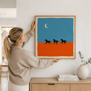 Horse Silhouette wall art held by a woman with a beige jumper above sideboard with books and a vase