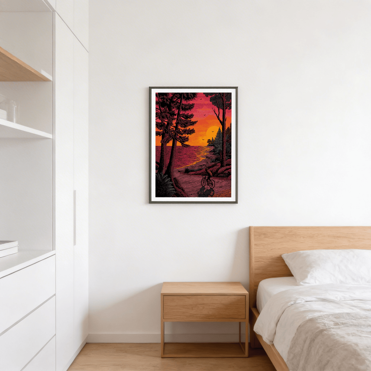 Bicycle Adventure print of a cyclist at sunset in red and orange hues on a bedroom wall above a wooden bedside table