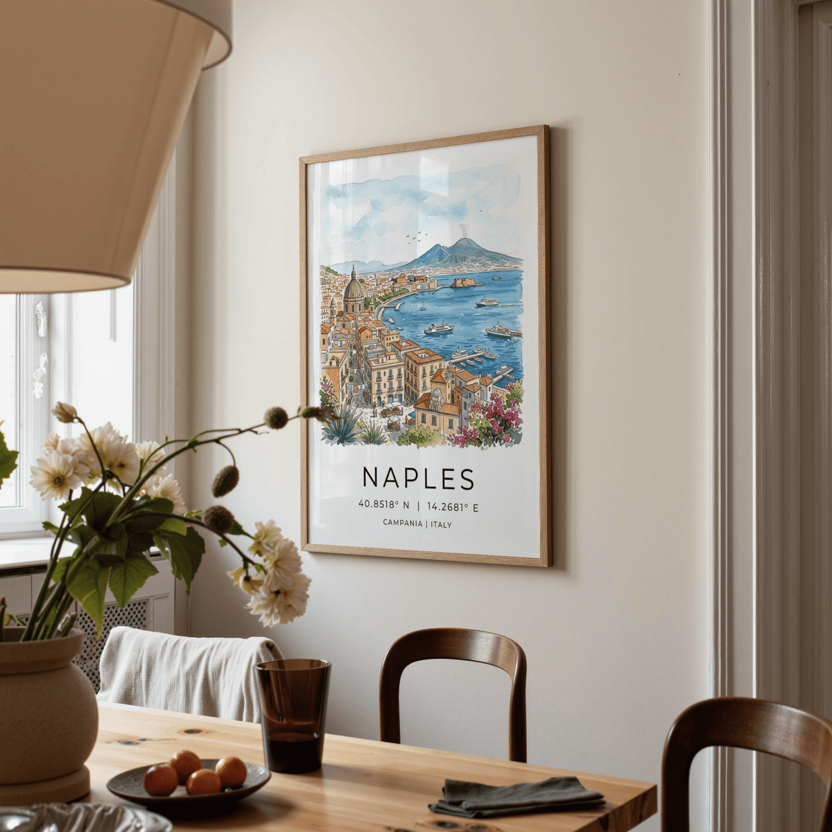Naples City Art Print on a cream wall above a dining table with flowers in a vase and a lamp