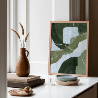 Framed Abstract Green Wall Art with green and blue abstract shapes on a white shelf near a brown jug and books