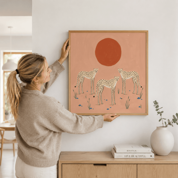 Framed cheetah art print with three cheetahs and a large red sun held on a living room wall above wooden furniture