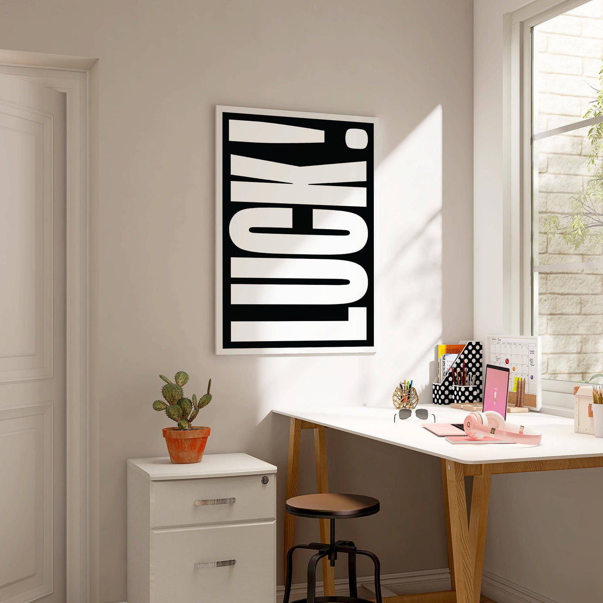Lucky Gifts wall art with white text on black background in a sunlit study next to a cactus on a filing cabinet