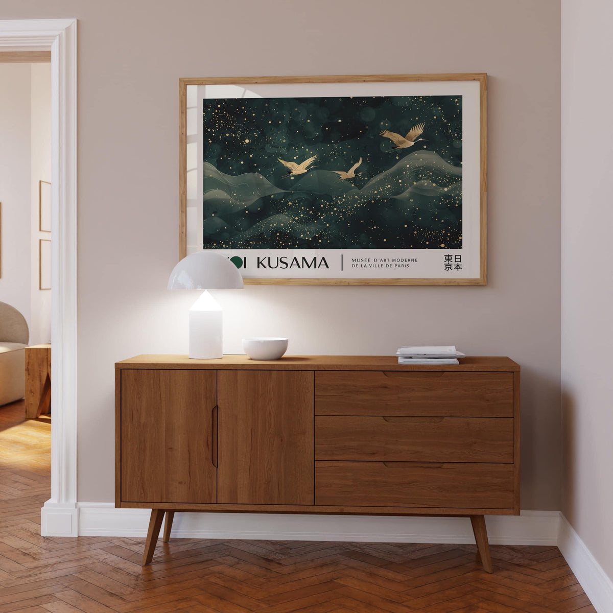 Japanese wall hanging of golden cranes flying over dark blue hills above a wooden sideboard with lamp