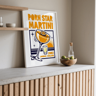 Print leaning on shelf of Passion Fruit Martini Print with orange and navy minimalist illustration beside a bowl of limes
