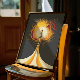 Framed Rocket Launch Art Print with bright yellow and orange retro illustration on a chair in a warmly lit room