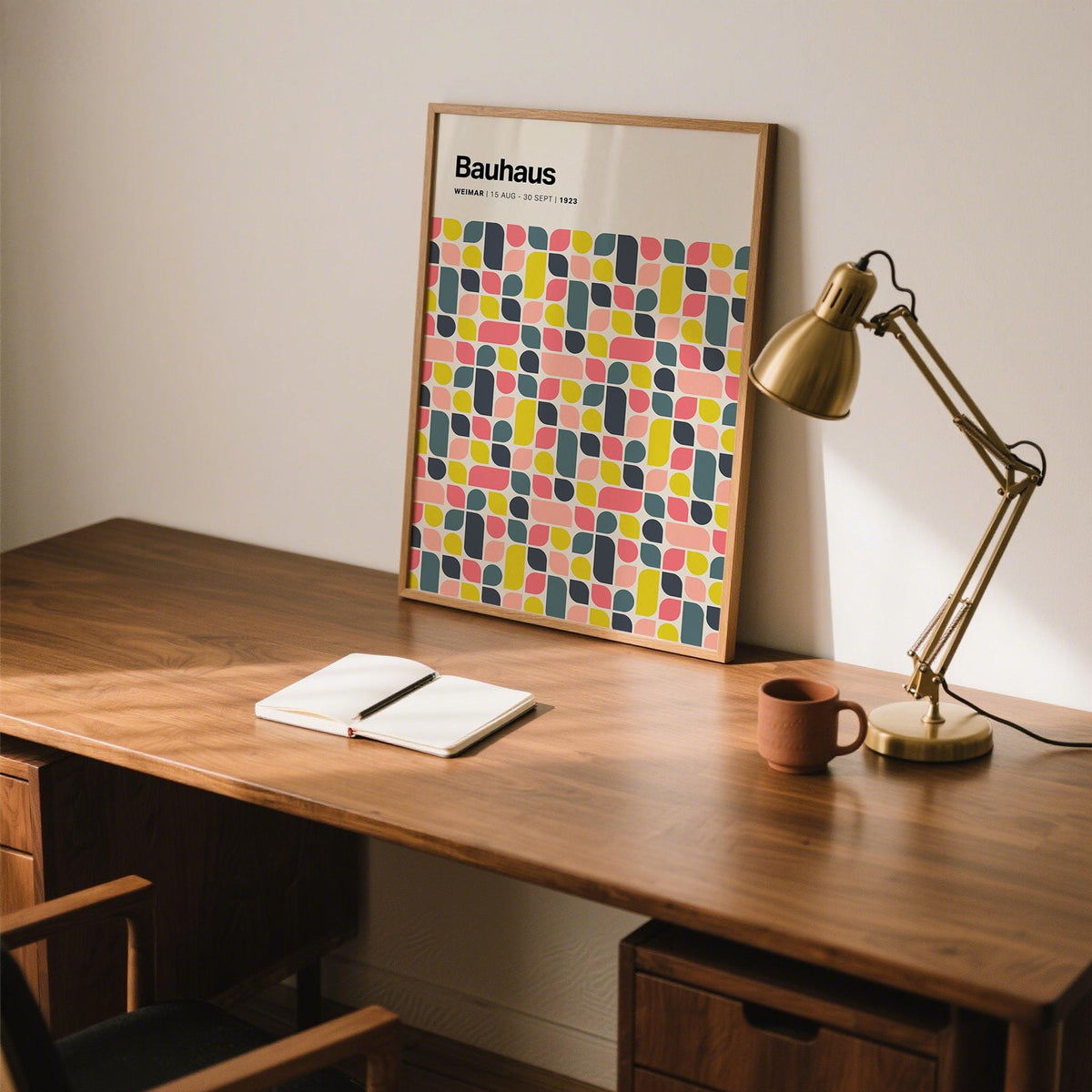 Colorful wall poster leaning on a wooden desk with a brown mug and gold desk lamp
