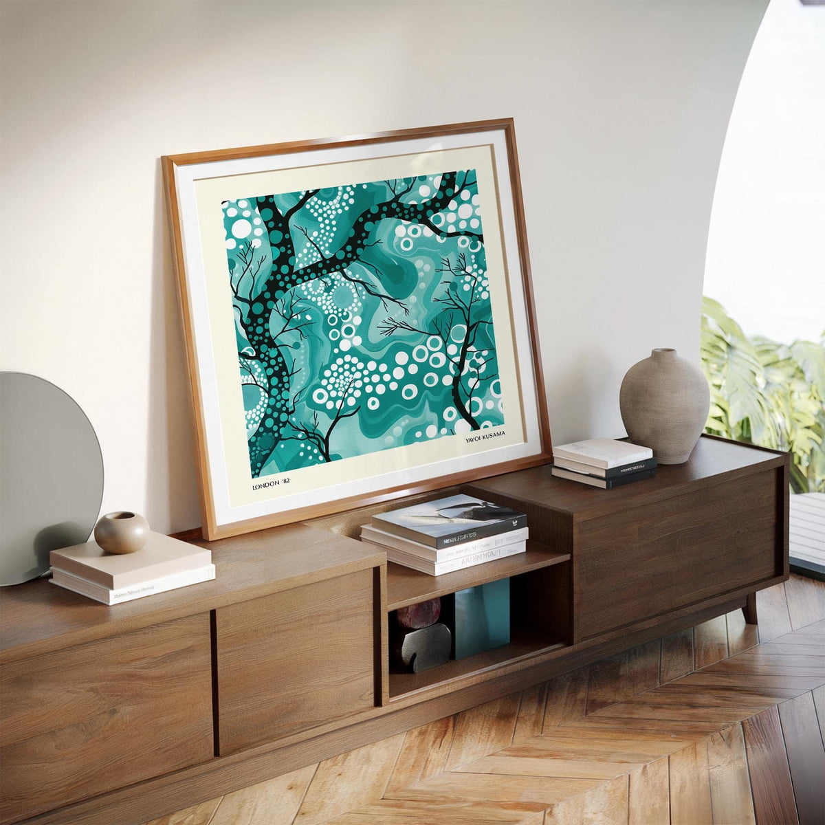 Print leaning on a wooden sideboard with teal abstract tree branches and white dots with a vase