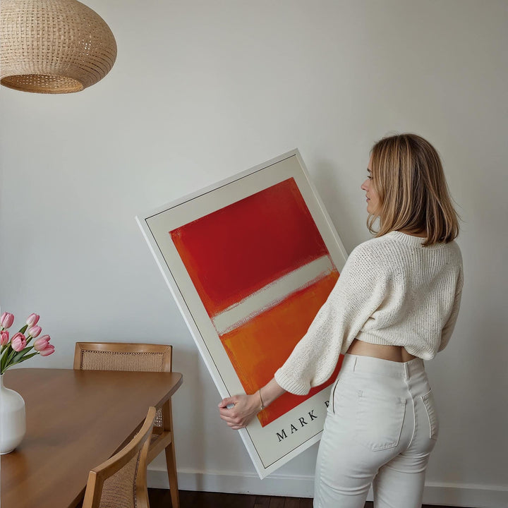 Framed Orange Abstract Art held by a woman near a dining table with pink tulips
