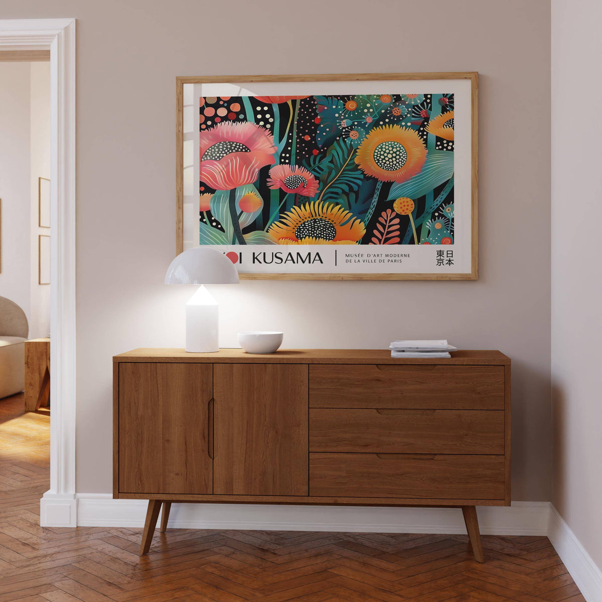 Floral wall art of kaleidoscope flowers in pink yellow and green above a wooden sideboard with a white lamp