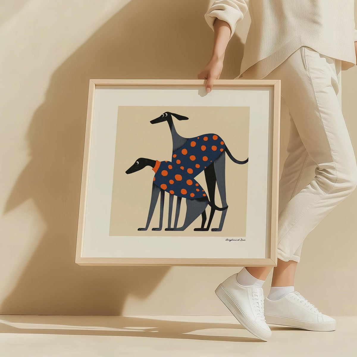 Framed poster of a dog with two greyhounds in blue coats with orange polka dots held by a person