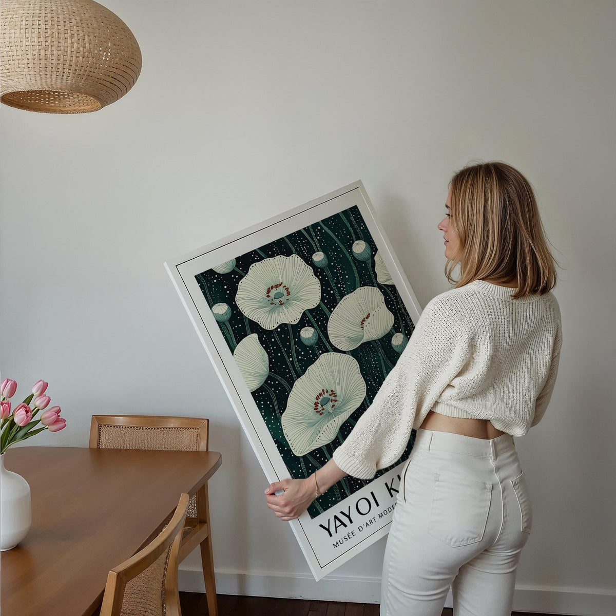 Framed Poppy Prints held by a woman featuring white poppy flowers on a dark green background with pink tulips nearby