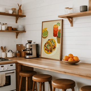 Print leaning on a kitchen counter of two tacos with toppings and a drink near bowls of guacamole and cactus