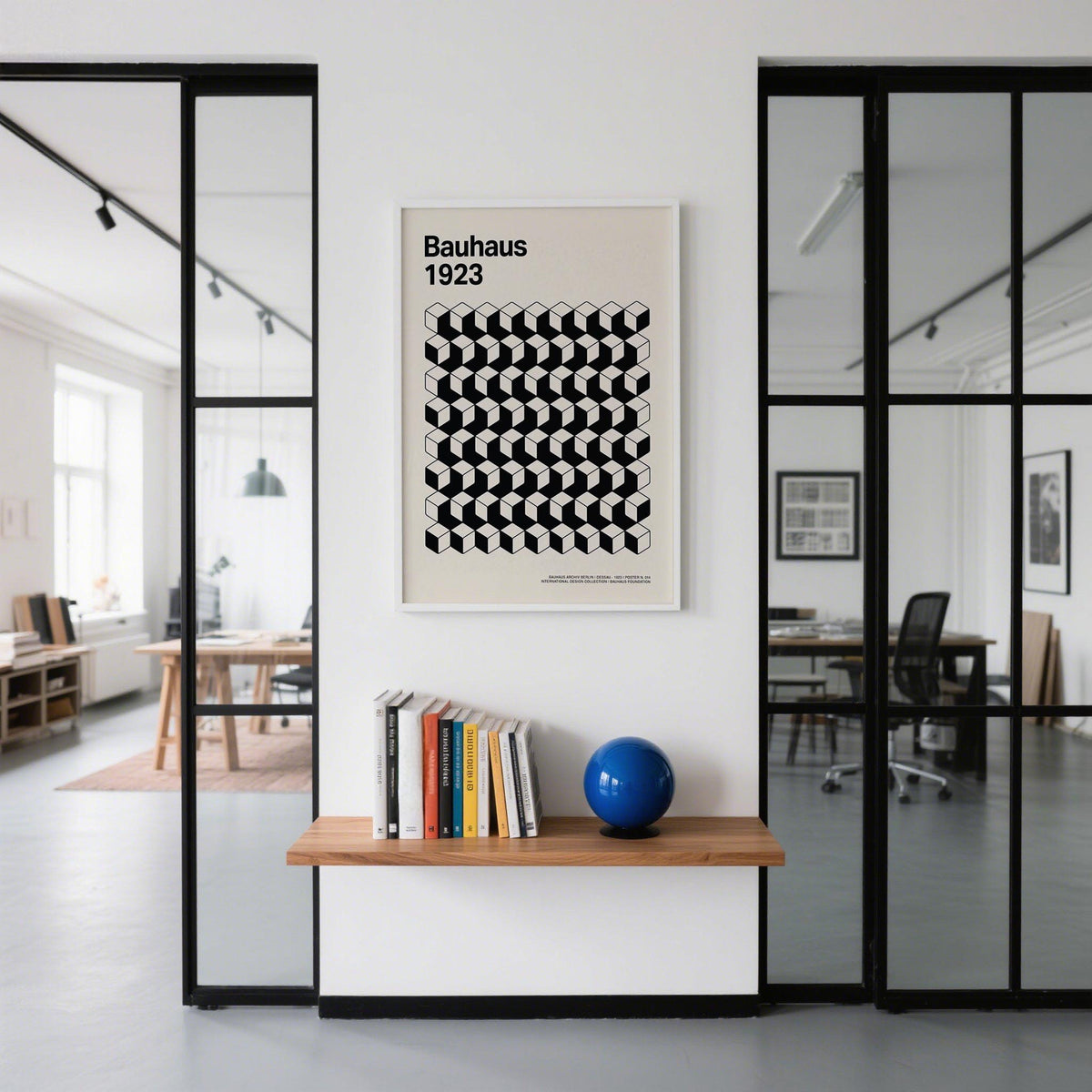 Print on a wall of Bauhaus Design showing black and white cubes in a minimalist office above a shelf with books and a blue ball