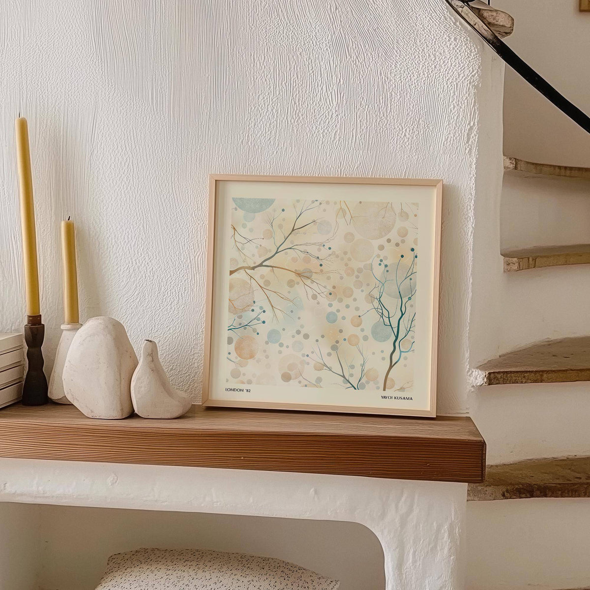 Neutral artwork leaning on a wooden shelf showing delicate branches with blue and beige berries with candles nearby