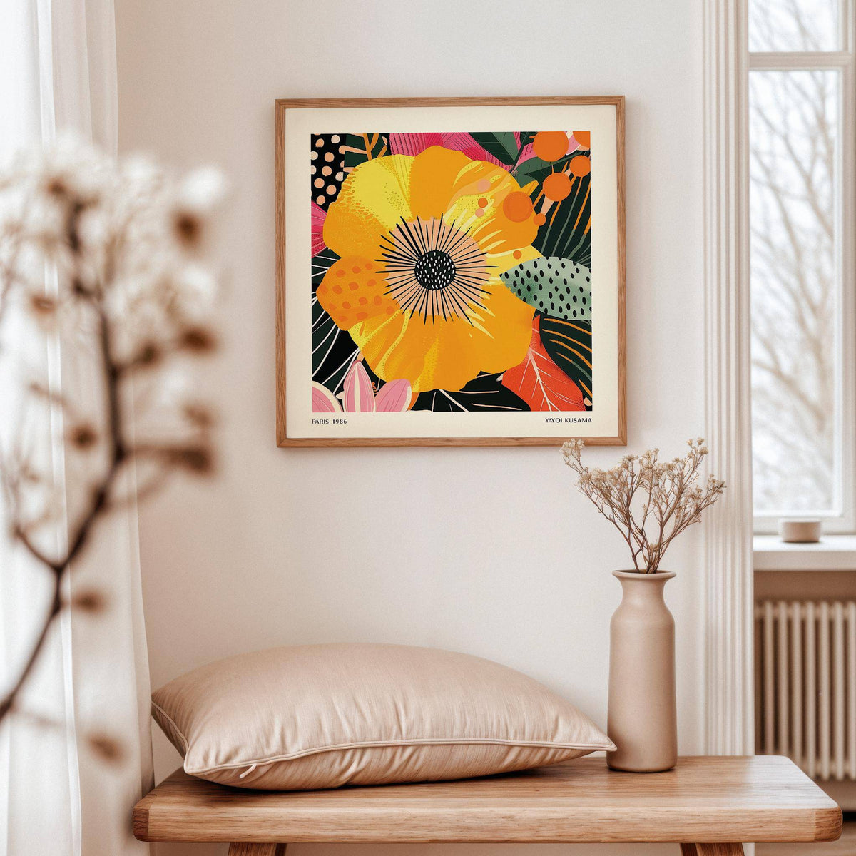 Yellow flower art print with pink and green leaves above a wooden table with a beige cushion and vase