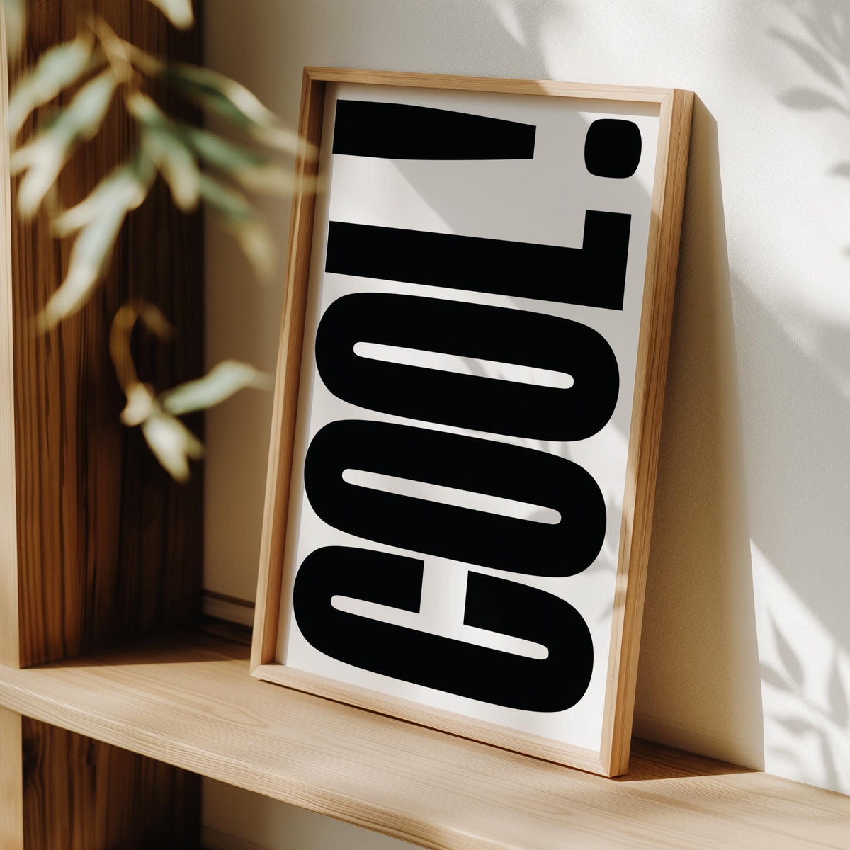 Framed Cool Typography Poster with bold black text leaning on a wooden shelf with sunlight and leaves nearby