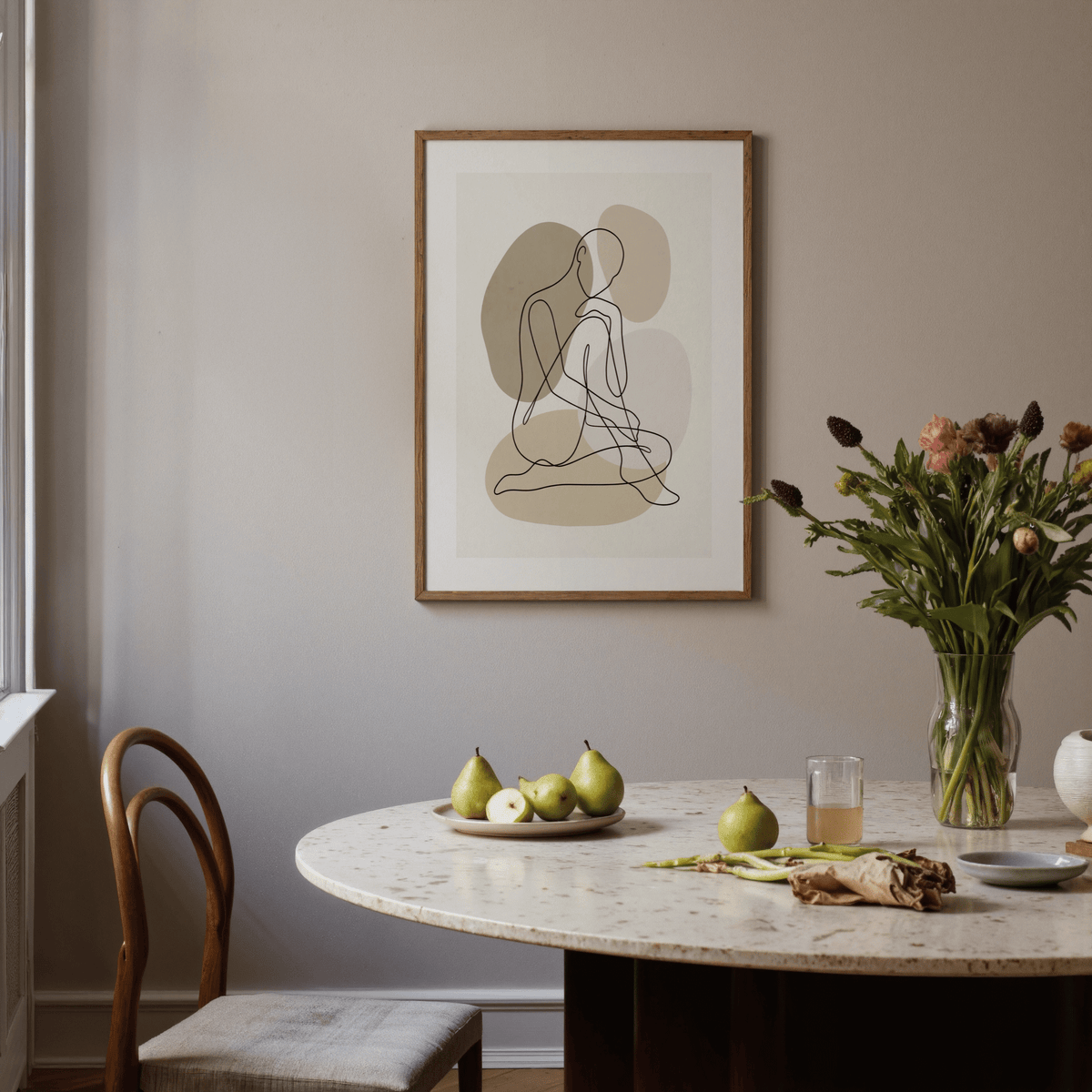 Line Art Figure Print framed on a beige wall above a round table with pears and flowers