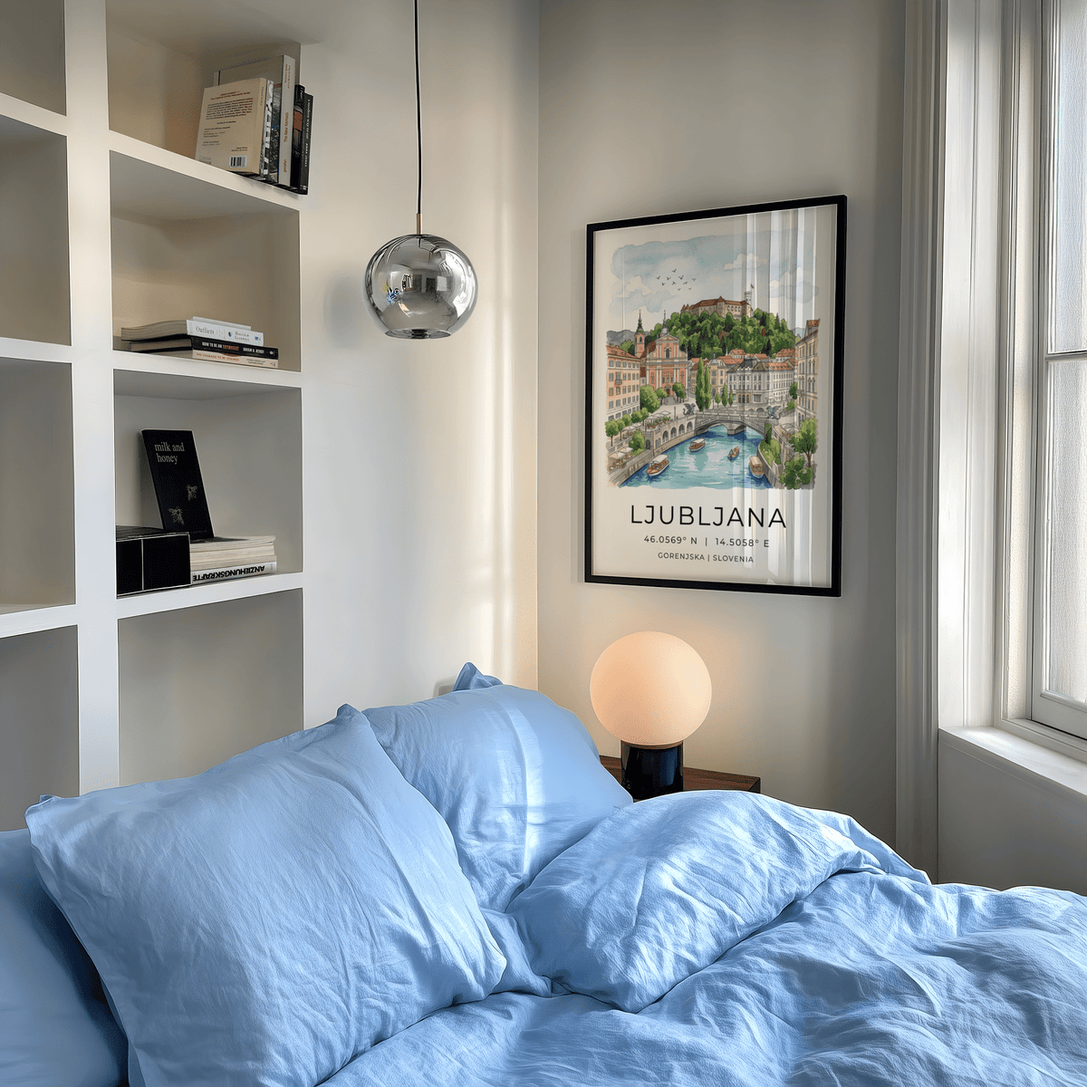 Ljubljana art print framed on a white wall above a bed with blue linen and a glowing lamp
