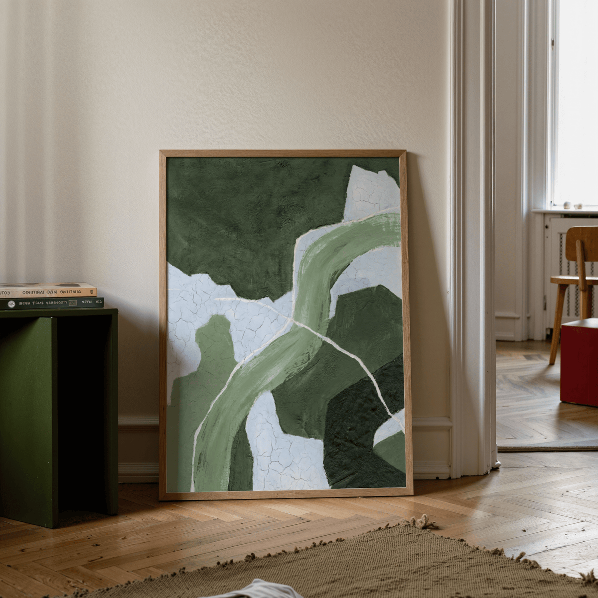 Abstract green art print leaning on floor with green side table and books nearby