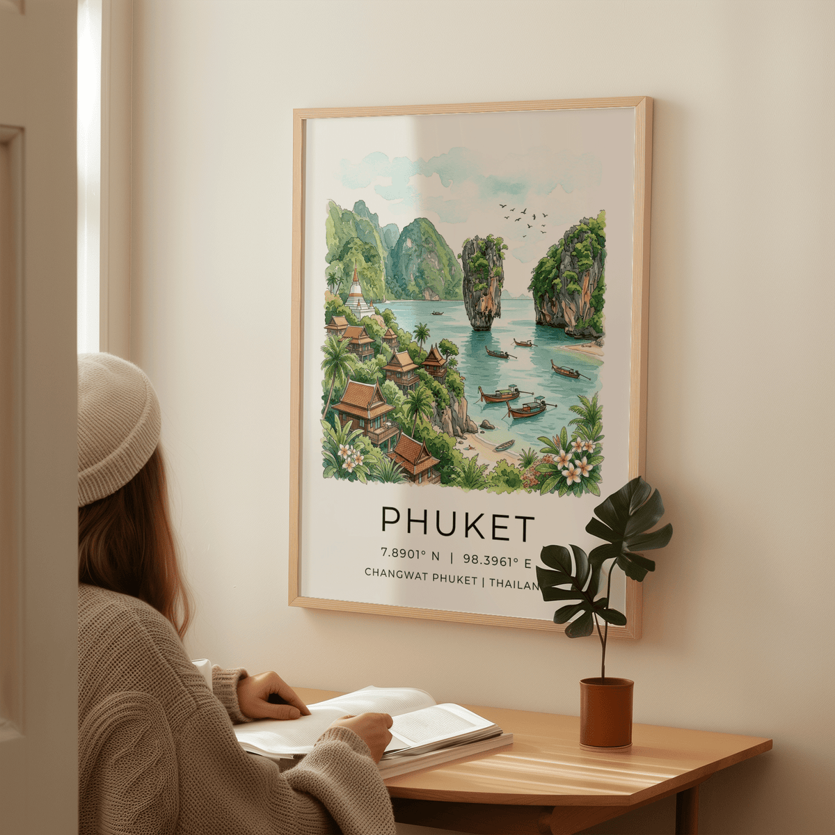Print on a wall of Phuket beach bay with turquoise water and green islands above a wooden desk with a plant