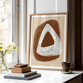 Print leaning on a windowsill with white and brown abstract triangle shapes near books and a cup